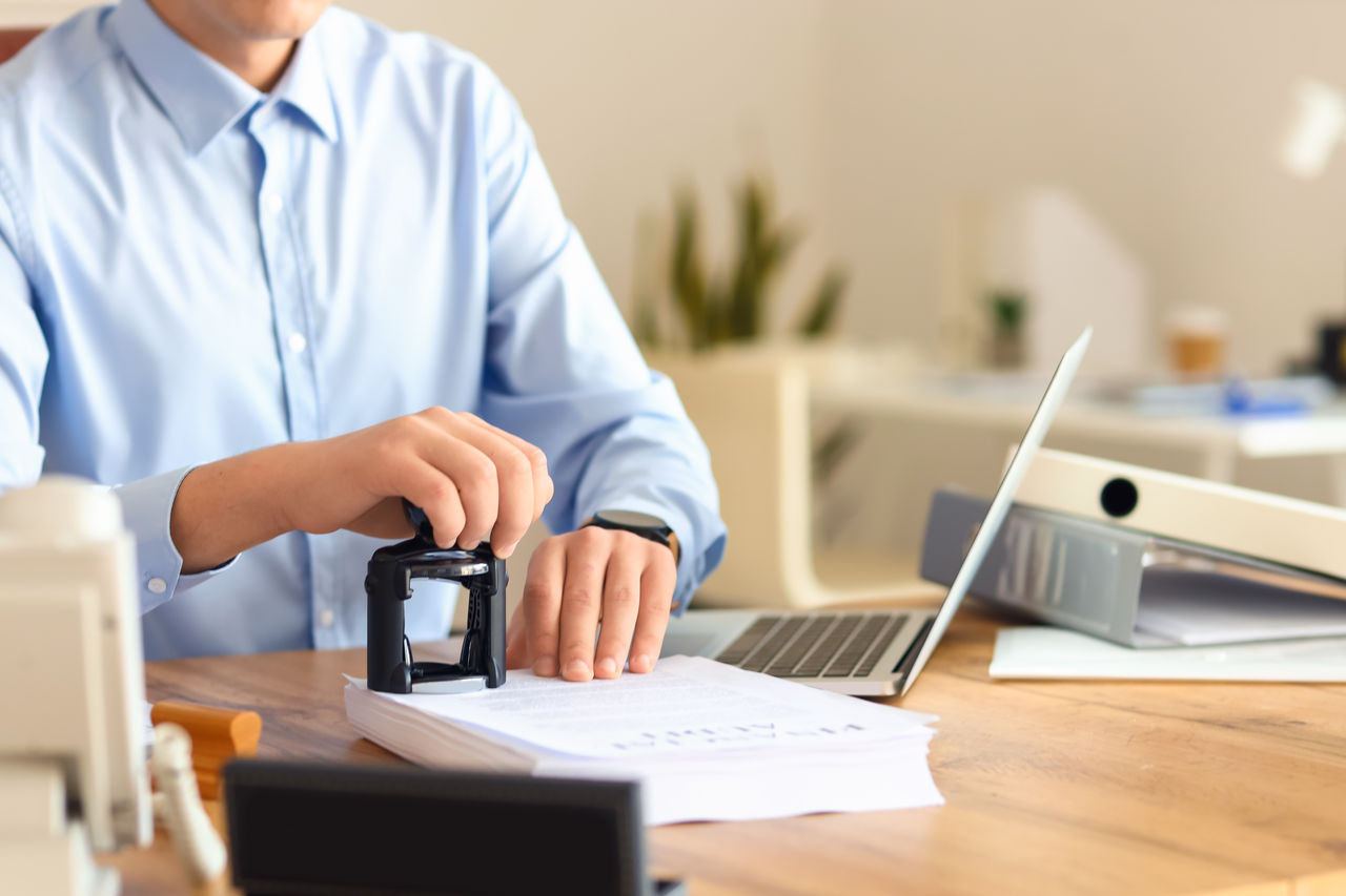 Young male notary public attaching seal to documents in office